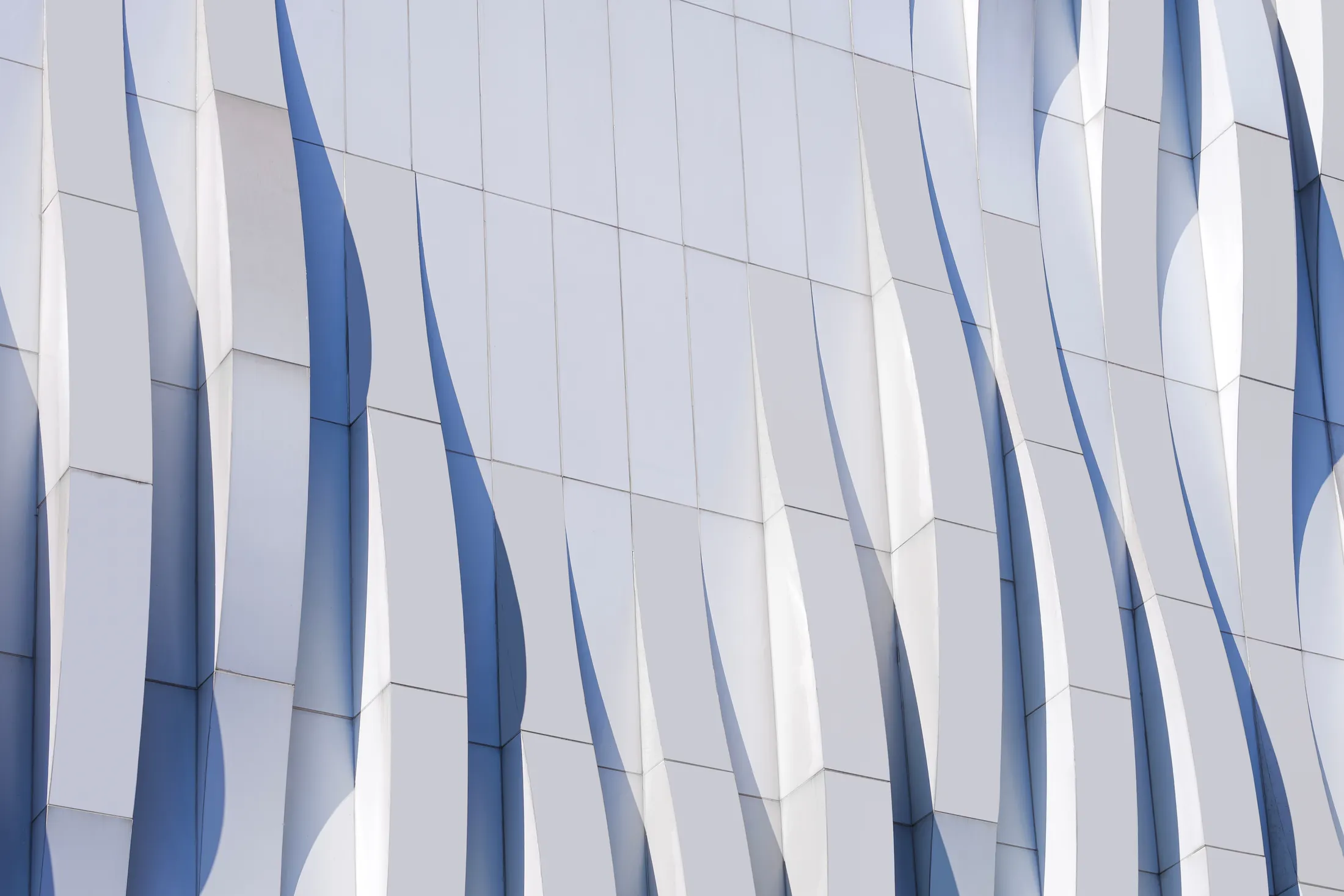 A pale facade of curved vertical fins running across a regular grid of flat panels.