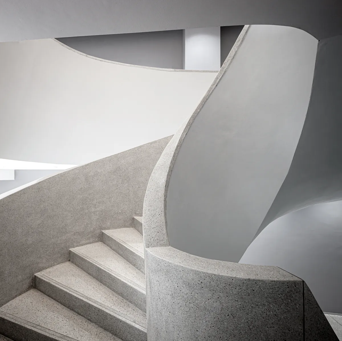 A curved terrazzo staircase winding up through a pale stairwell.