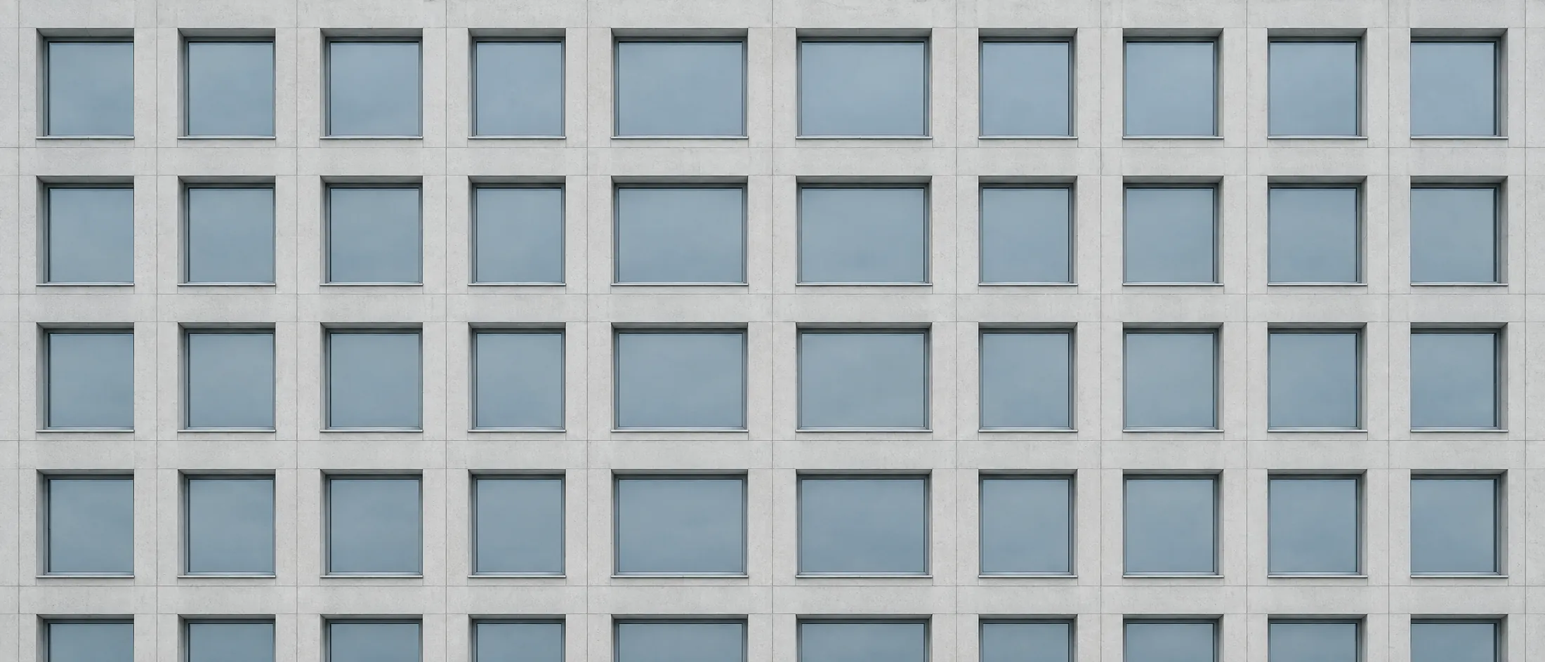 A building facade of identical rectangular window openings in an exact repeating grid.