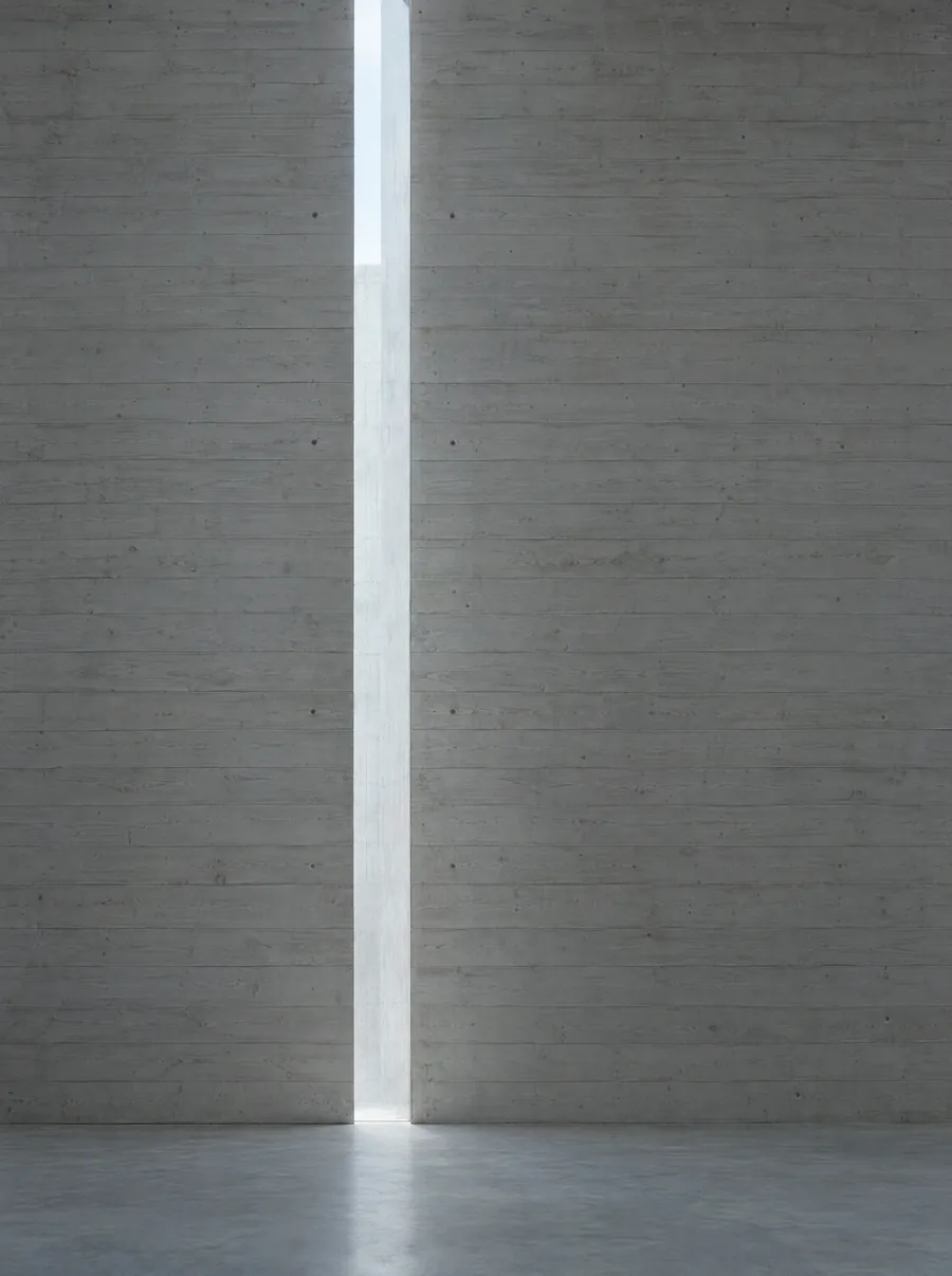 A narrow slot of daylight falling down a board-formed concrete wall.