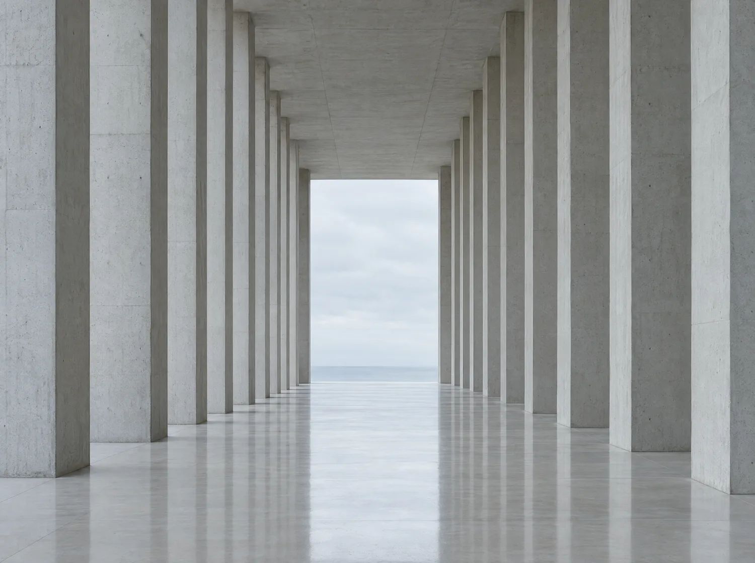 A long concrete colonnade receding toward a bright opening and a flat sea horizon.